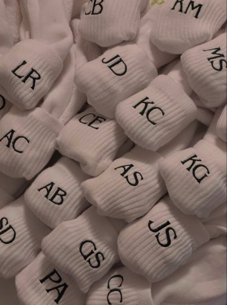 White ribbed socks with black embroidered initials piled together in a group.