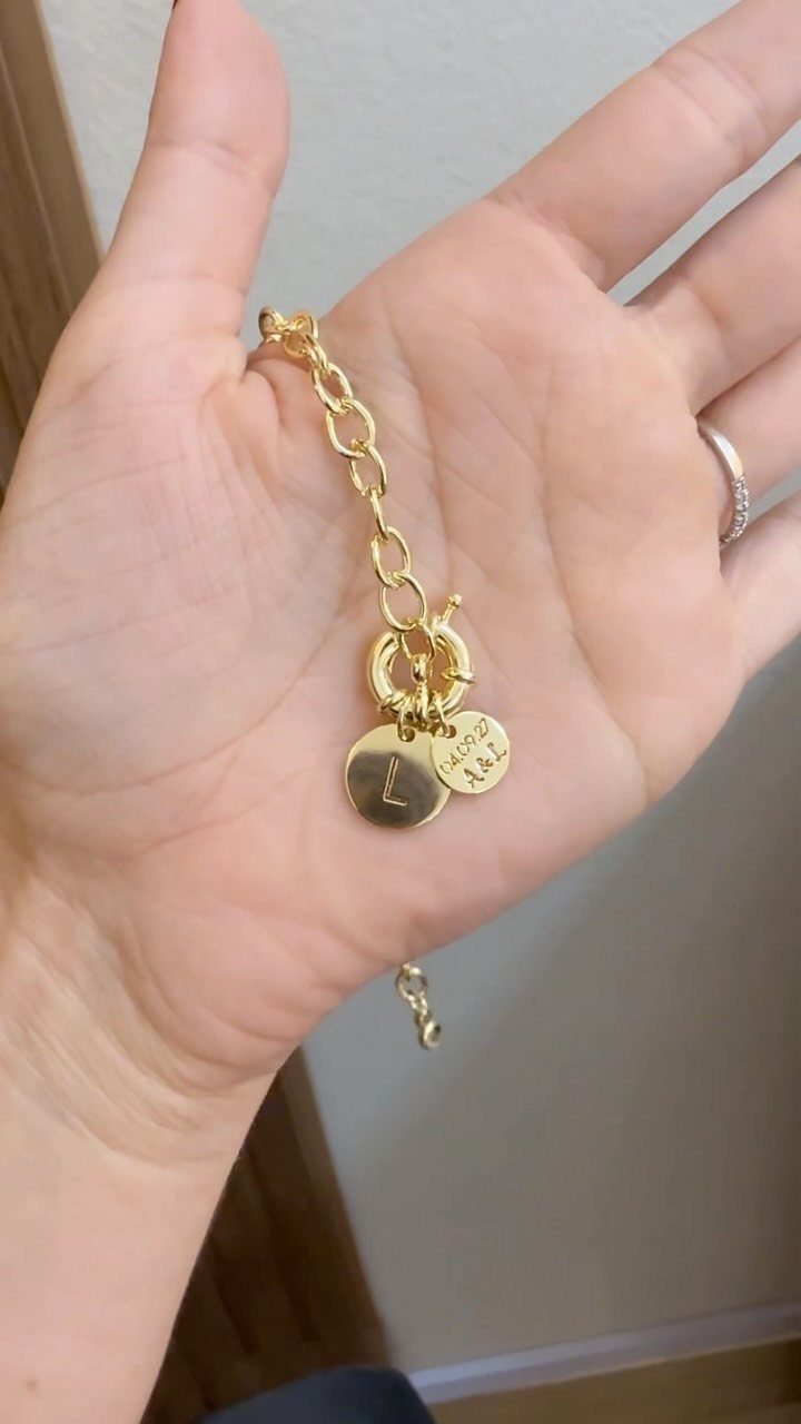 Gold chain bracelet with personalized letter and text charms held in a palm.
