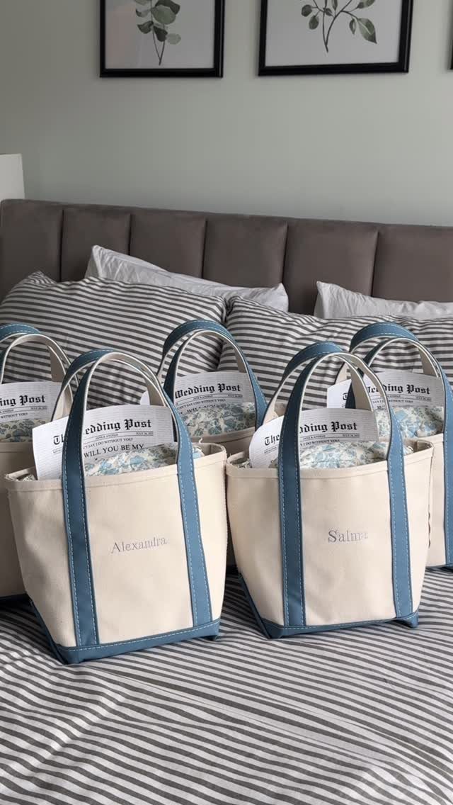 Personalized cream canvas tote bags with blue handles arranged on a striped bed.