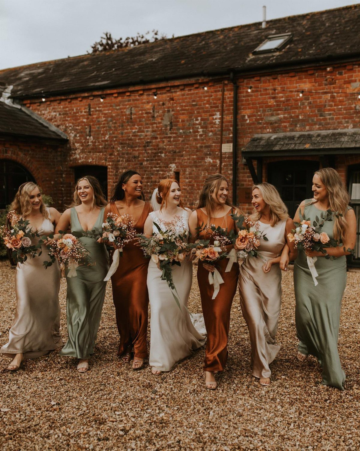 Bride and bridesmaids in champagne, sage, and copper satin dresses walking outdoors.