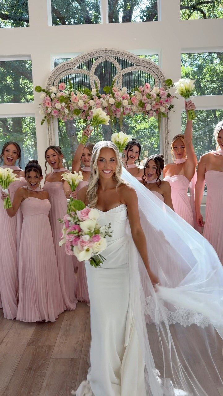 Bride in white gown surrounded by bridesmaids wearing dusty rose colored dresses.