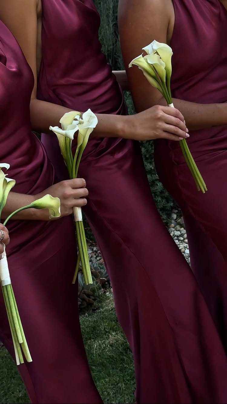 Women in deep purple satin bridesmaid dresses holding white calla lily bouquets.