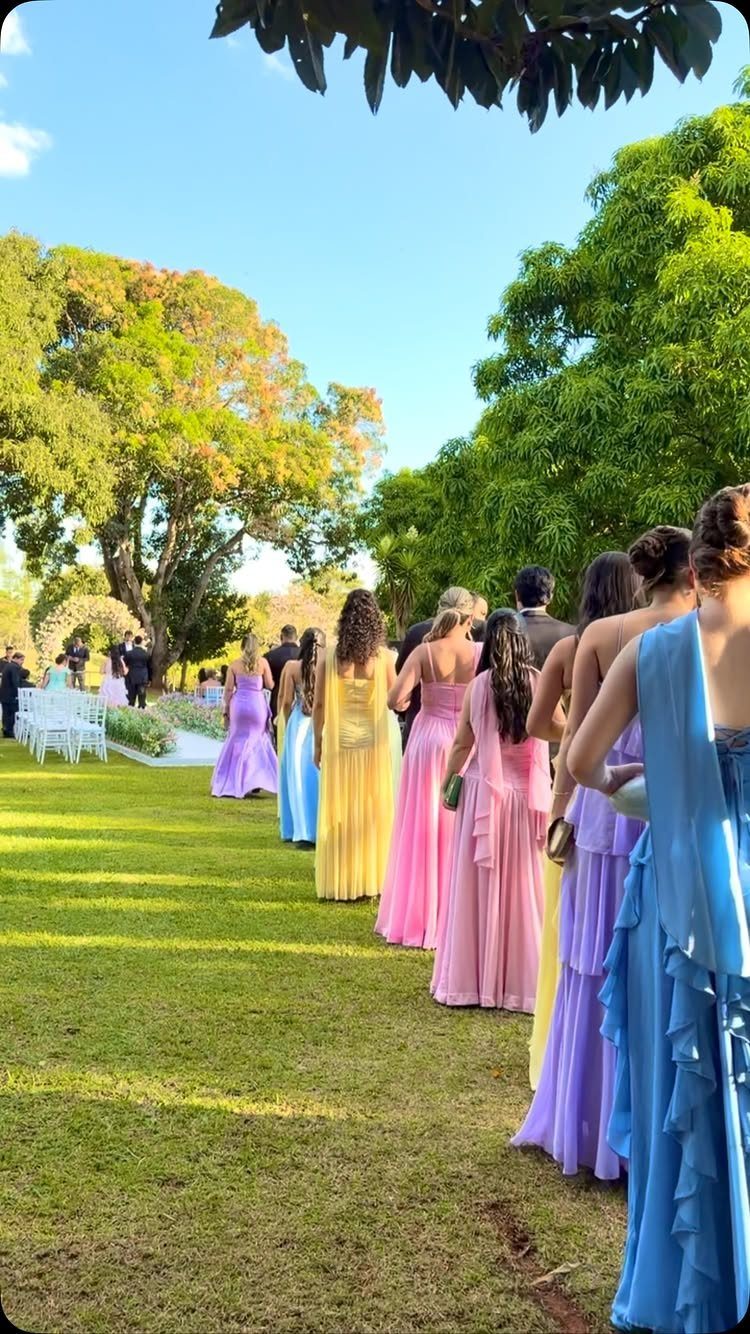 Bridesmaids in colorful pastel gowns standing in a line on a sunny lawn.