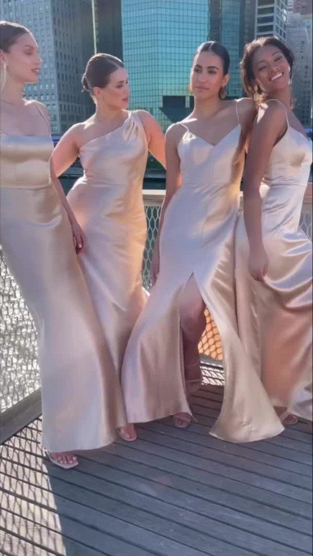 Four women wearing shimmering champagne-gold satin bridesmaid dresses on a city rooftop deck.