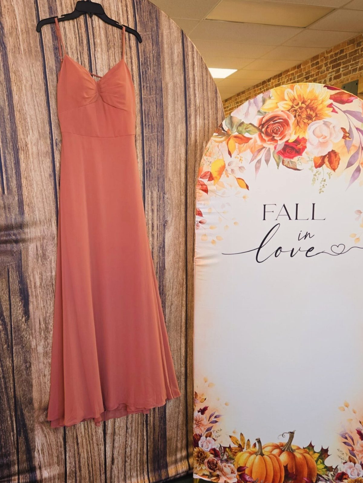 Terracotta bridesmaid dress hanging against a rustic wood background next to autumn decor.