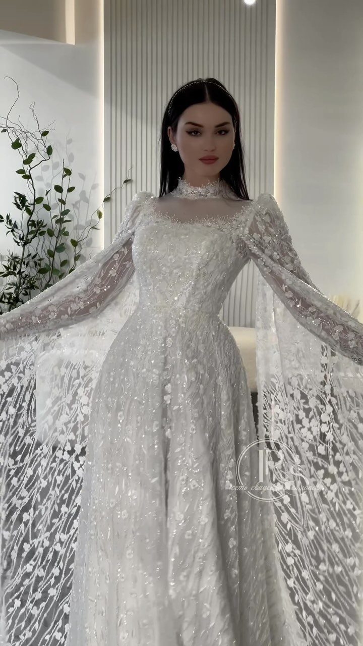 Woman in a white sparkling wedding gown with long sheer lace cape sleeves.