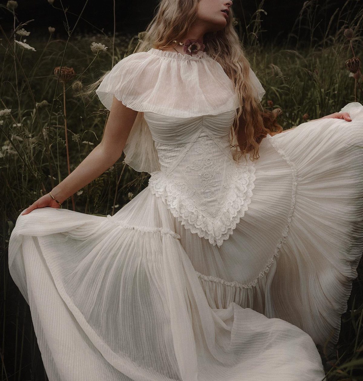 Woman in a white wedding gown with a ruffled capelet in a field