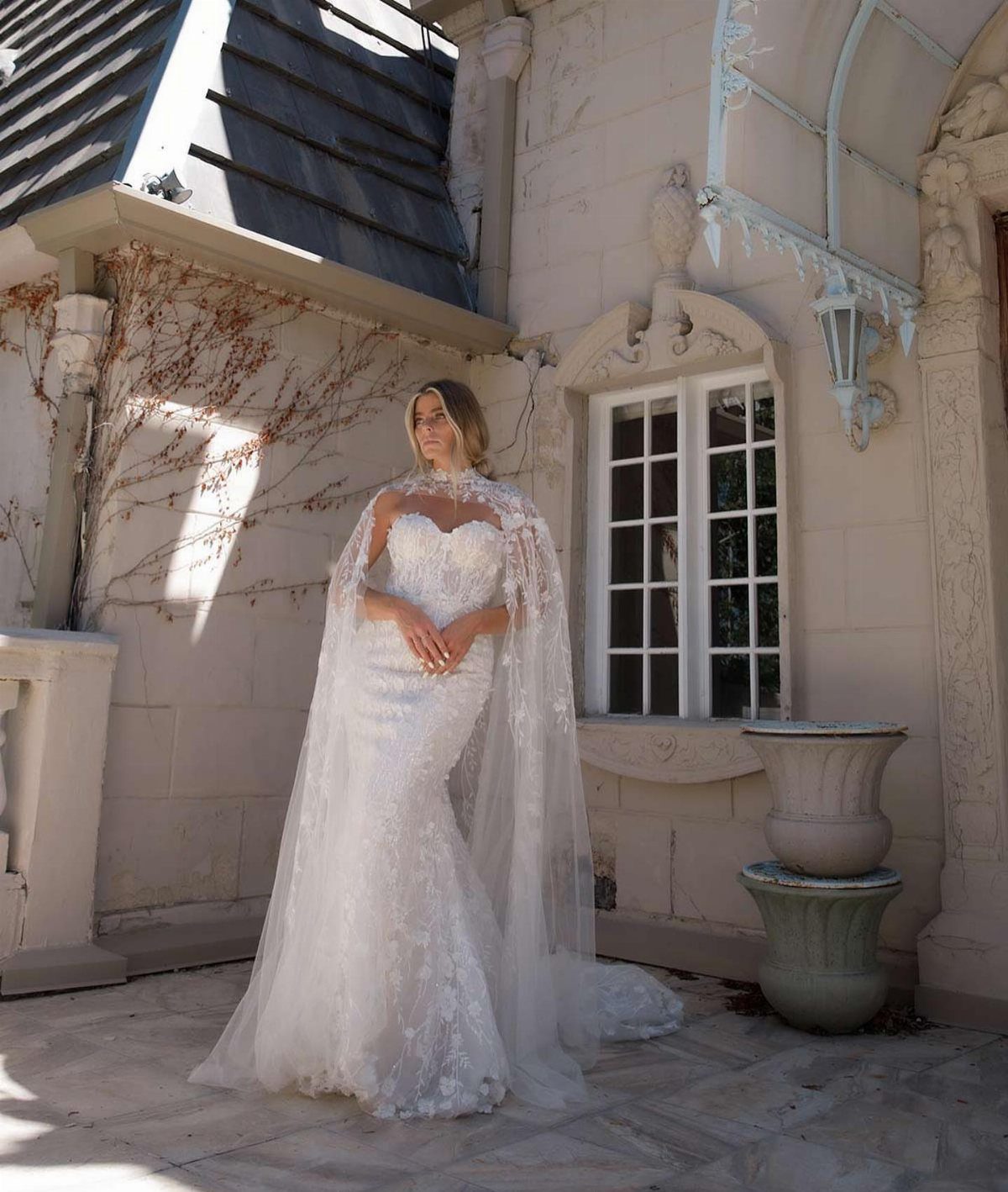 Woman in a white lace wedding dress with a long sheer lace cape.