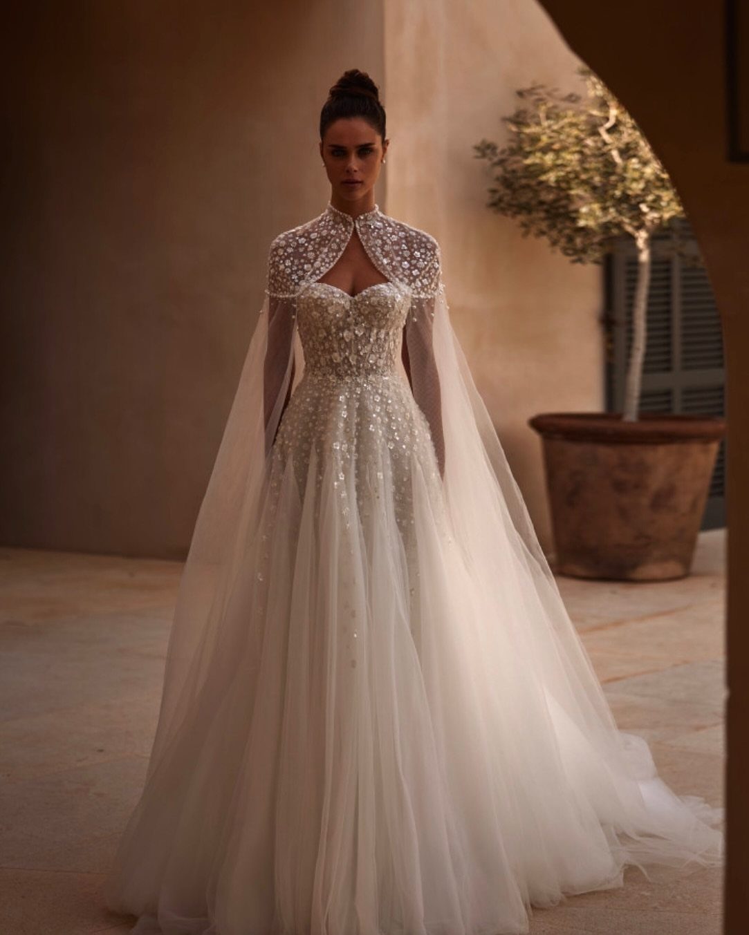 Woman in a sparkly white wedding dress with a matching embellished cape and train.
