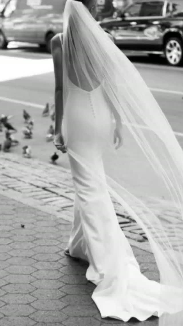 Woman in a minimalist white wedding gown and long veil walking on city street