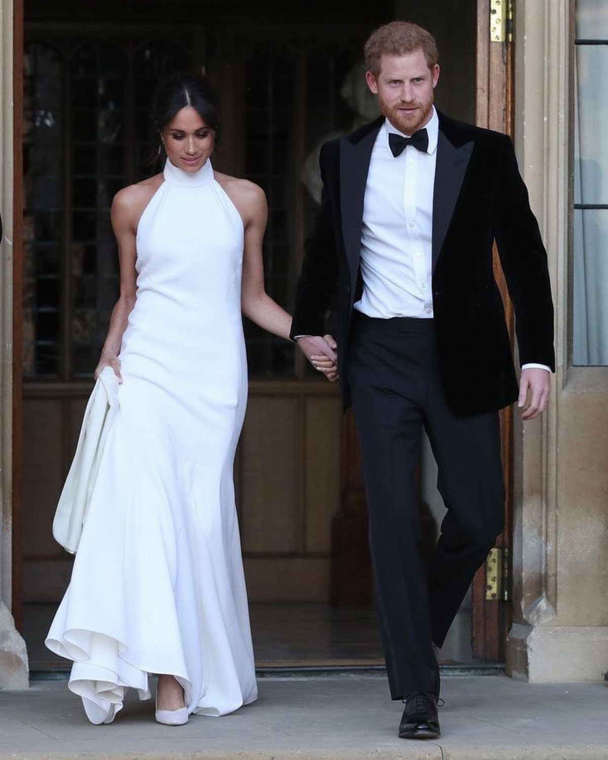 Woman in white halter wedding dress and man in tuxedo walking hand-in-hand.