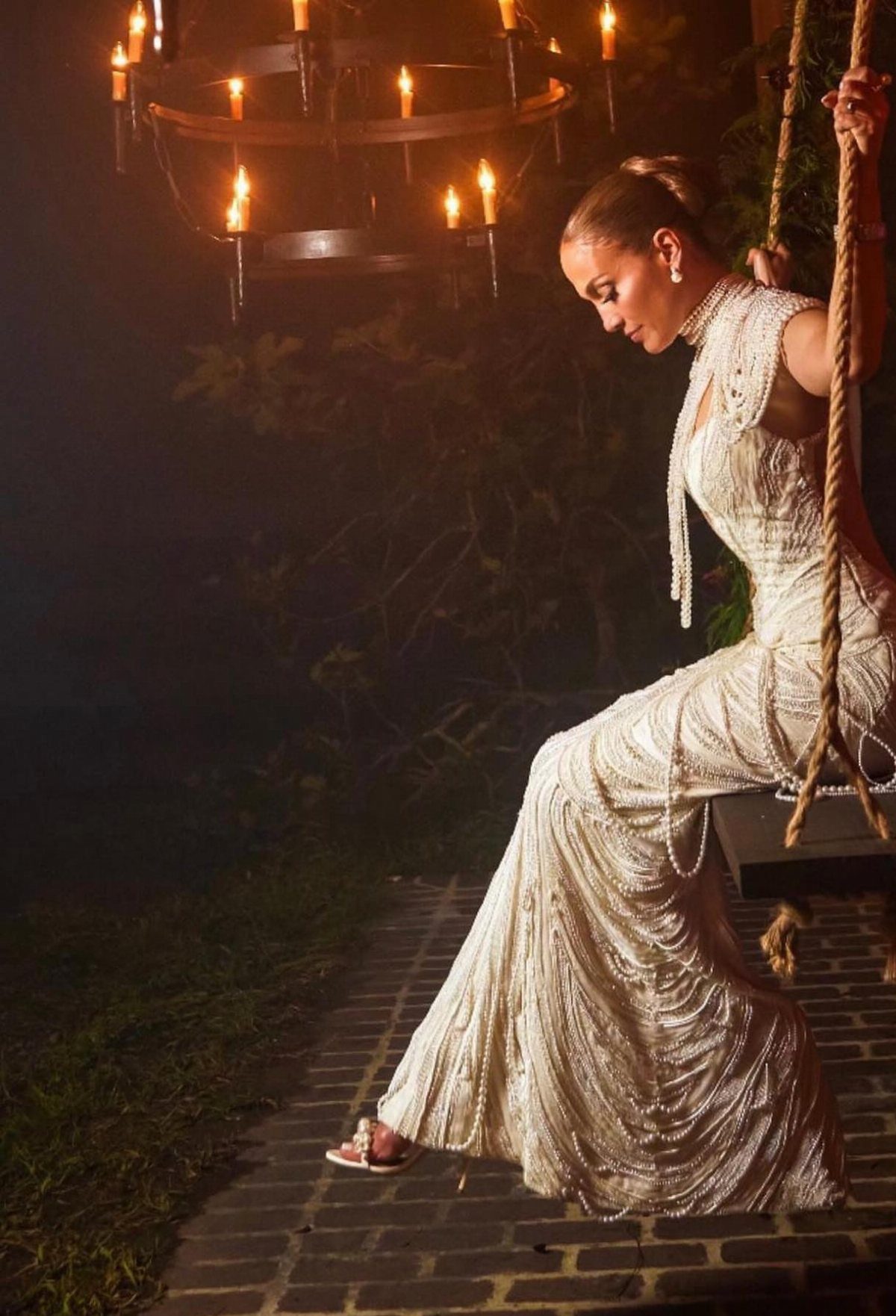Woman in a beaded white wedding dress sitting on a rope swing at night
