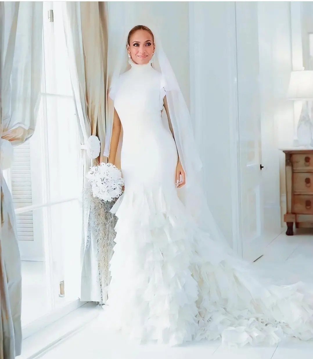 Woman in a white high-neck wedding dress with ruffled skirt and long veil.