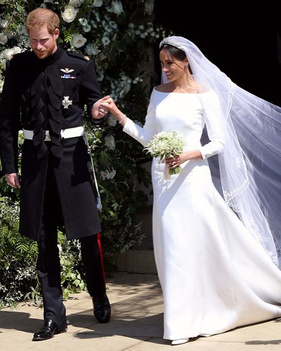 Meghan Markle wearing her white Givenchy wedding dress and veil walking with Prince Harry.