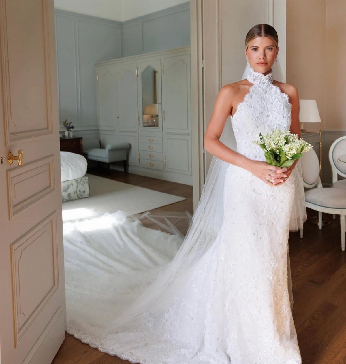 Woman in a white lace high-neck wedding dress holding a bouquet of white flowers.