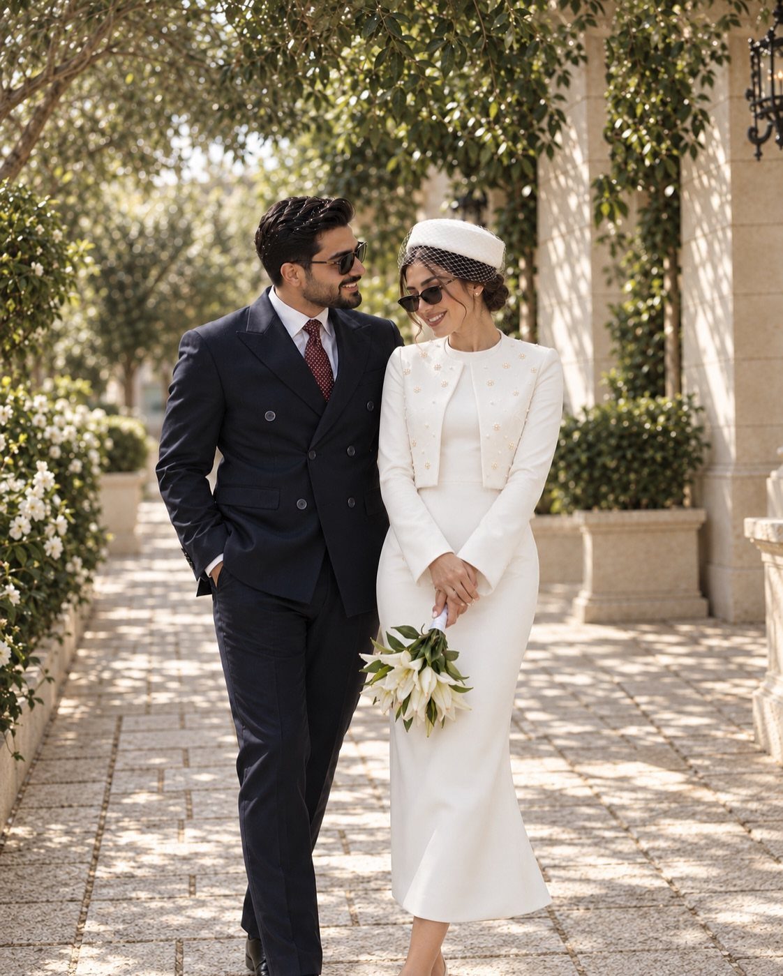 Bride in a white midi dress and structured jacket walking with groom.