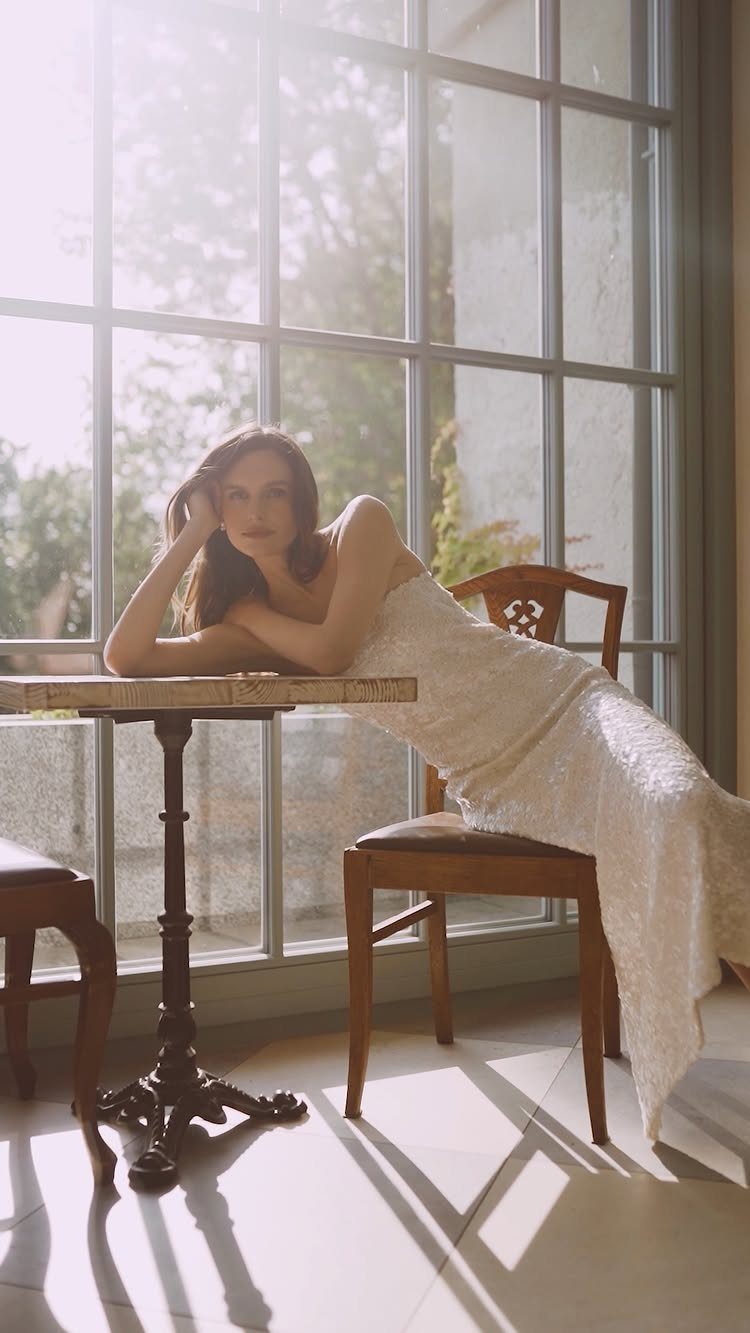 Woman in a strapless white lace bridal gown leaning on a marble table.