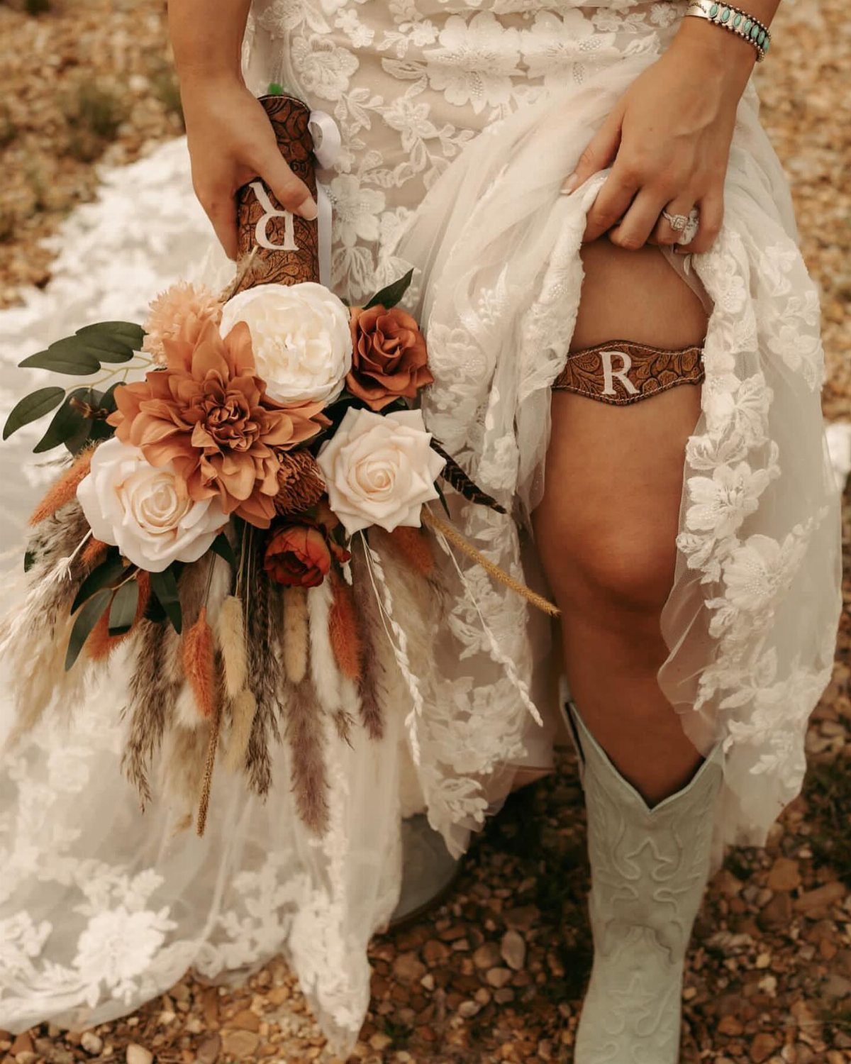 Bride in lace wedding dress and cowboy boots holding a rustic floral bouquet