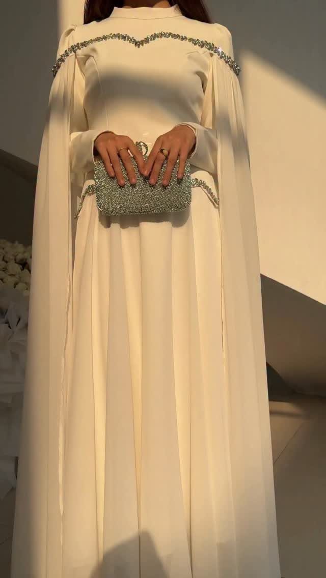 Person in a cream beaded gown with cape sleeves holding a silver clutch