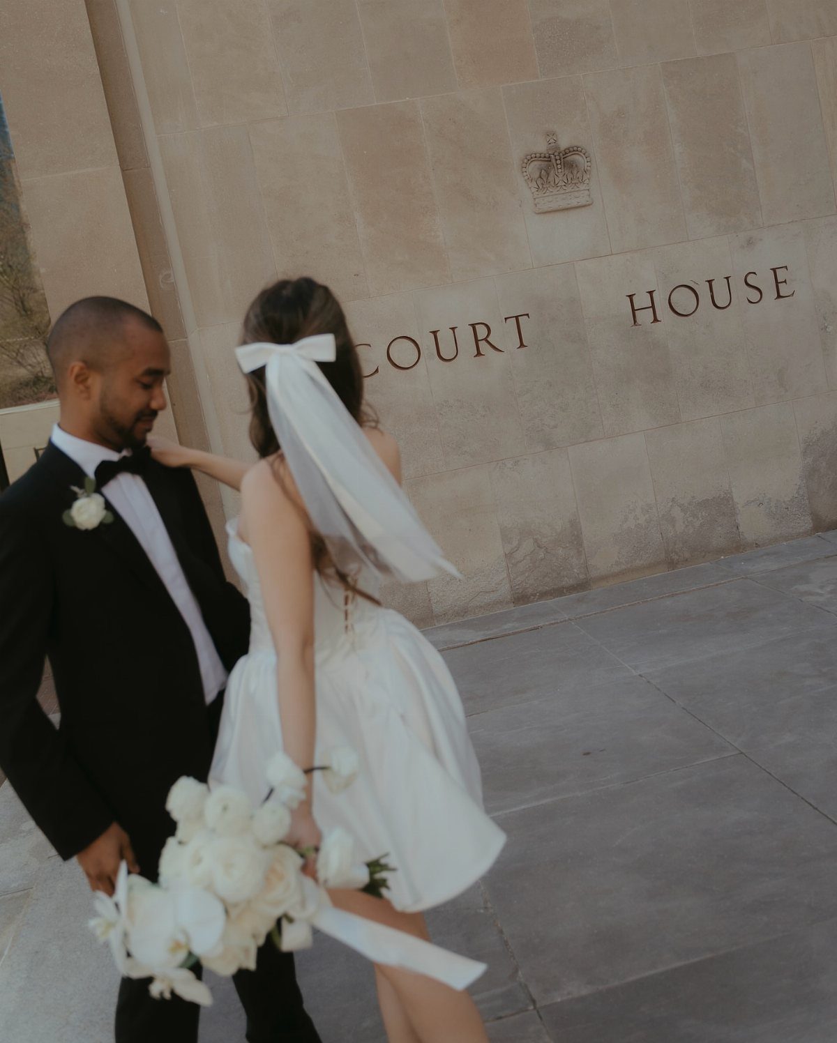 Bride wearing a short white veil and dress standing with groom at courthouse.