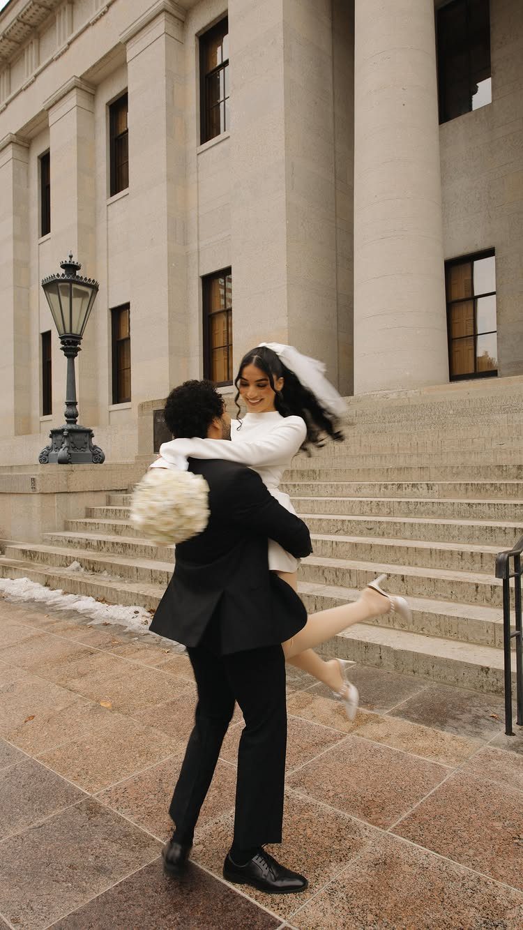 Couple in wedding attire embracing in front of a stone courthouse building