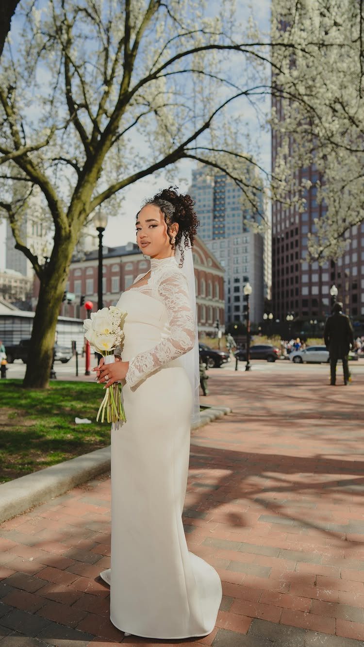 Woman in a white lace long-sleeved wedding gown holding white flowers in a park