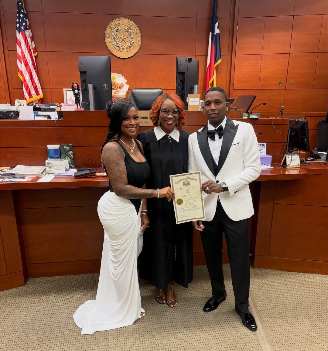 Couple and officiant posing with a marriage certificate in a wood-paneled office.