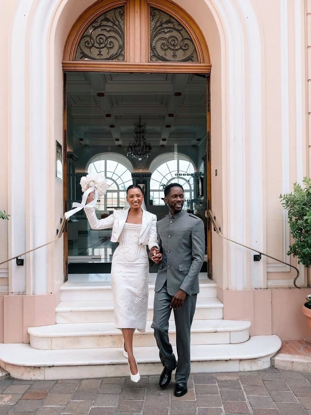 Couple in white dress and grey suit posing on marble steps outside building