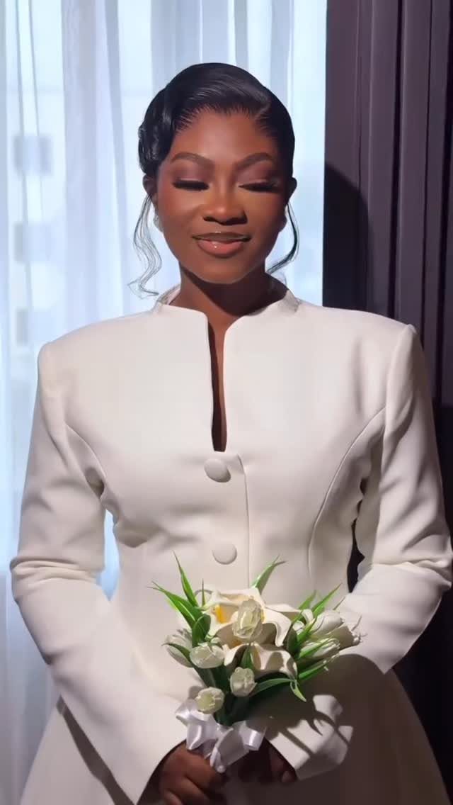 Woman in a structured white long-sleeved wedding dress holding a white lily bouquet.