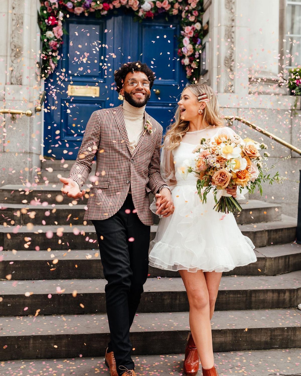 Couple walking down steps with confetti, woman wearing a short ivory wedding dress.