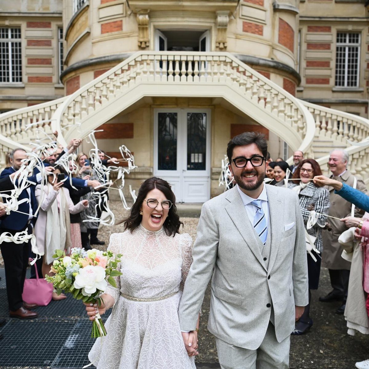 Bride in ivory lace wedding dress and groom in grey suit walking together.