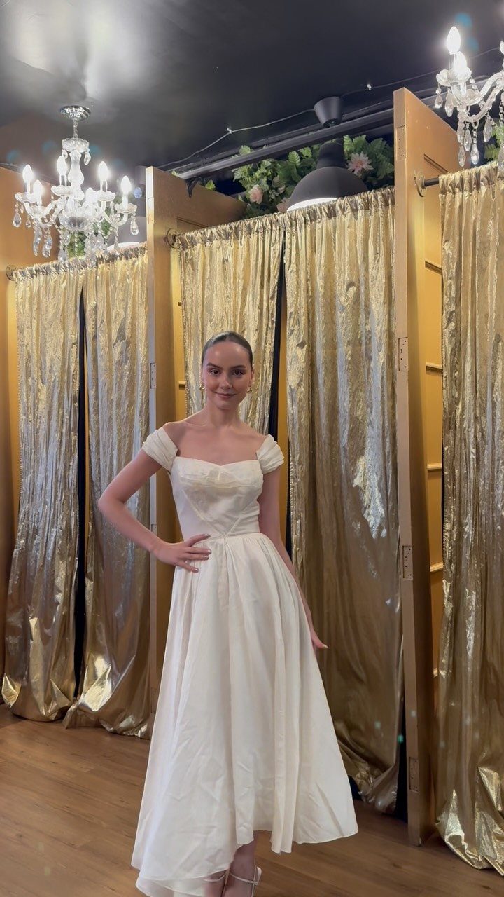 Woman in a white satin midi wedding dress posing in a bridal boutique.