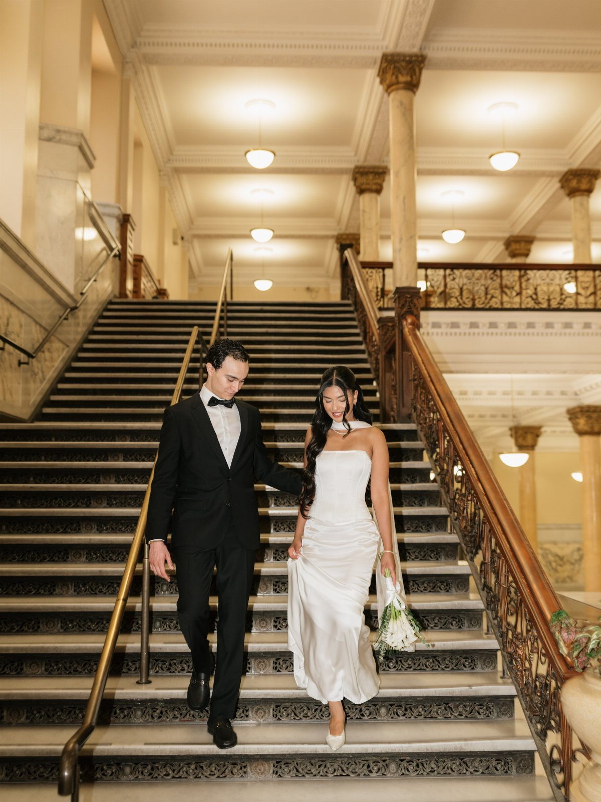 Bride in a simple white strapless dress and groom in a tuxedo on stairs