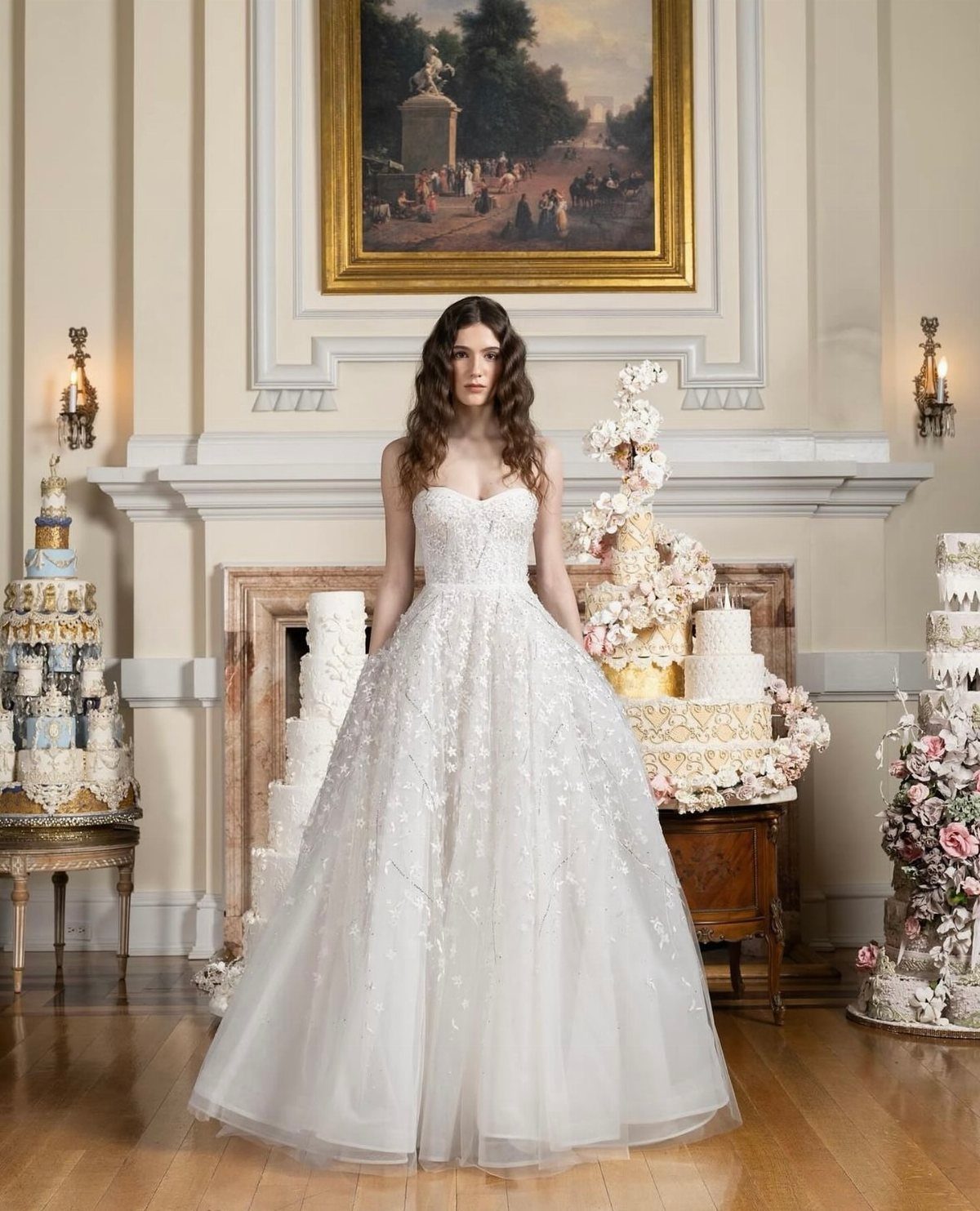 Woman in a strapless white beaded bridal gown standing among tiered wedding cakes.