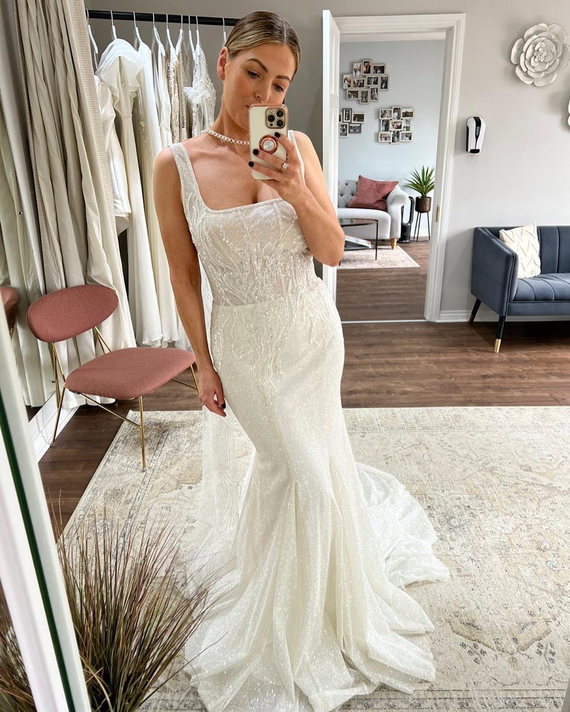 Woman in a beaded white mermaid wedding gown taking a mirror selfie in boutique