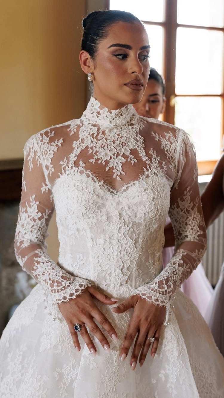 Woman in a white lace bridal gown with a high neck and long sleeves.