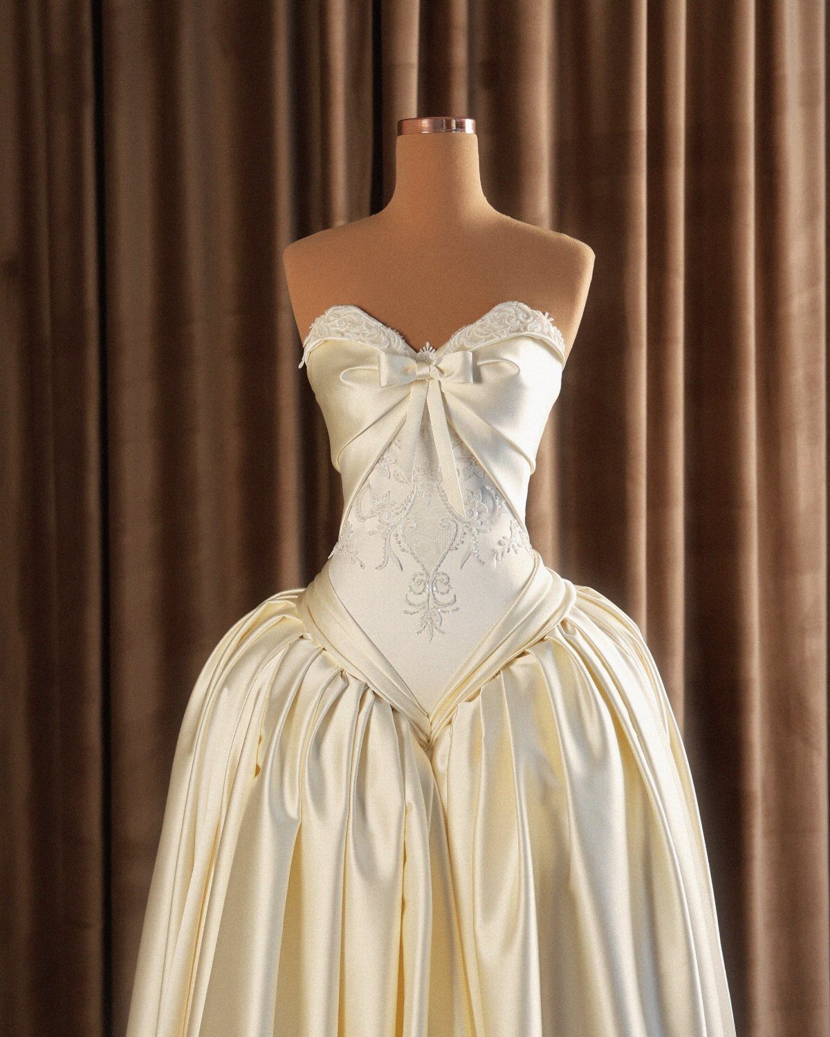 Cream satin bridal gown with a voluminous skirt on a mannequin against curtains