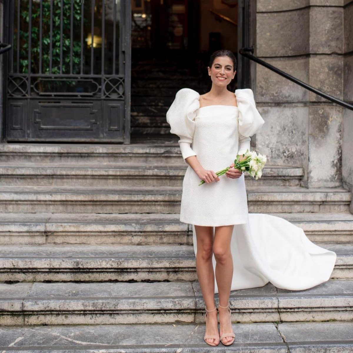 Woman in a short white bridal gown with puff sleeves and long train.