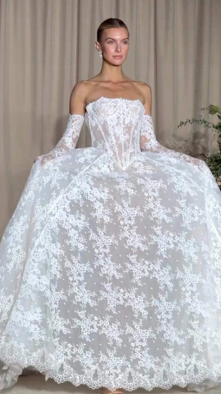 Woman in a voluminous white lace bridal gown with matching lace gloves.