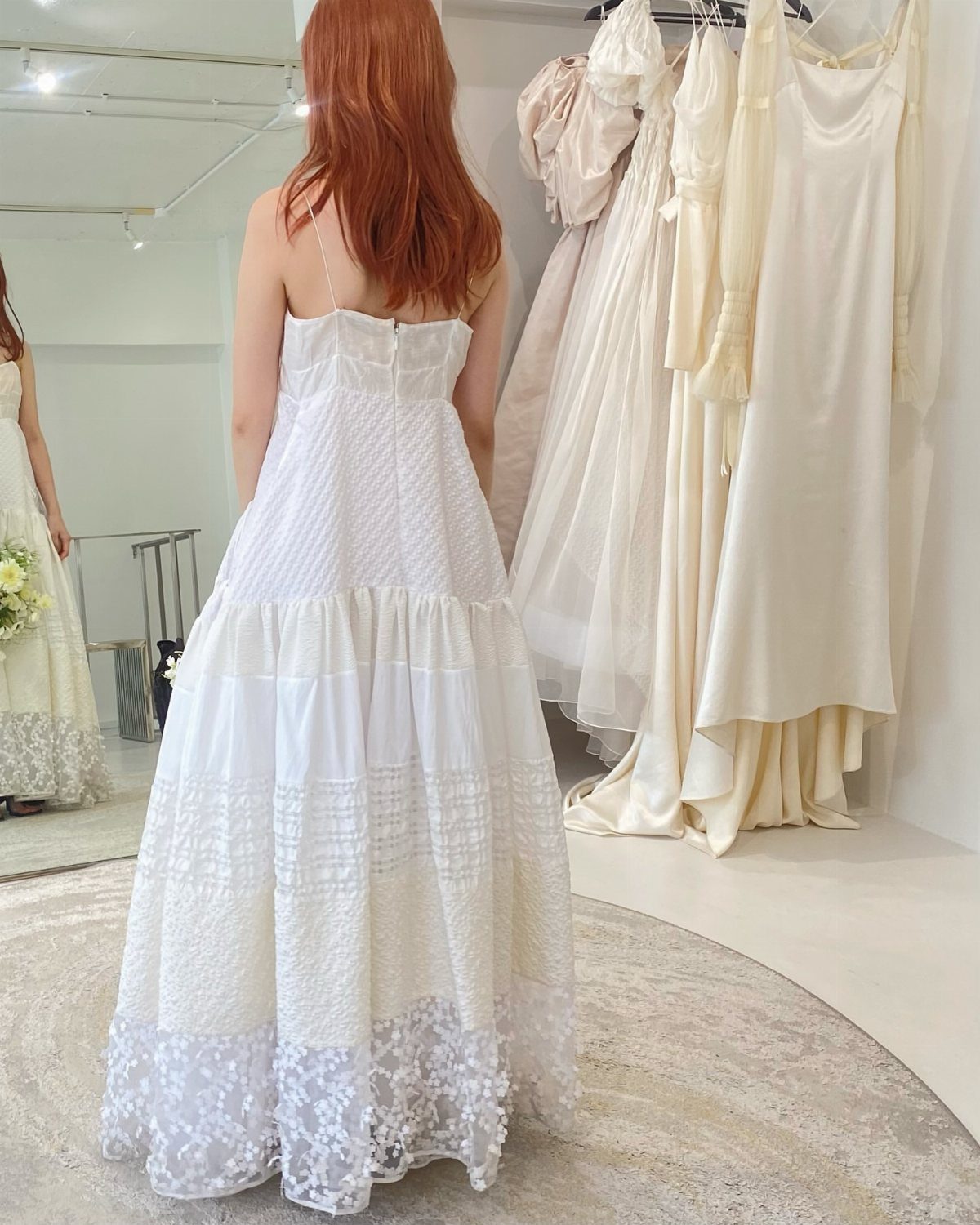 Woman from behind wearing a voluminous white tiered bridal gown in a boutique