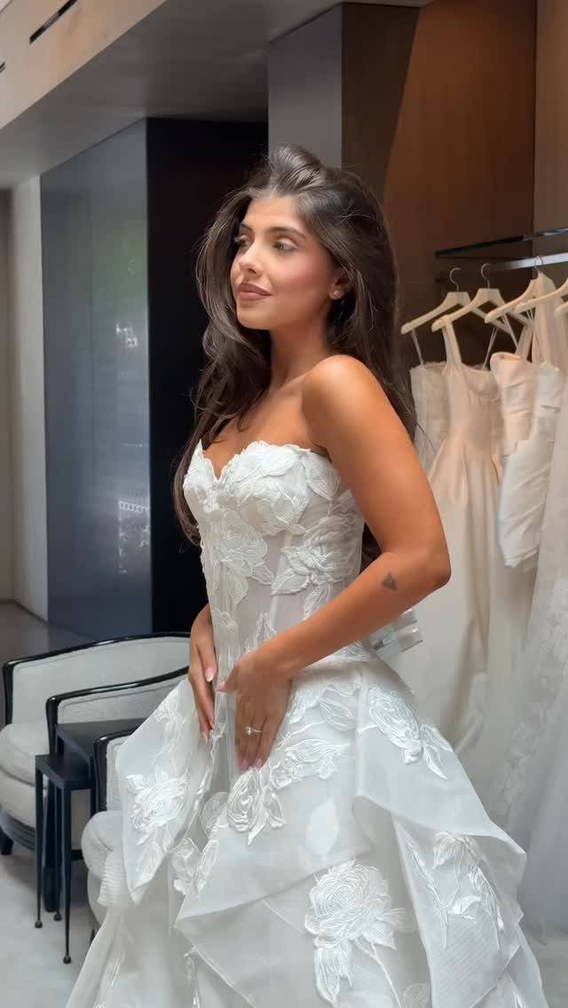 Woman wearing a strapless white bridal gown with 3D floral details in a boutique.