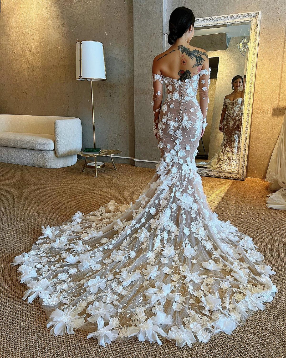 Woman wearing a form-fitting white wedding gown with 3D floral appliqués and long train.