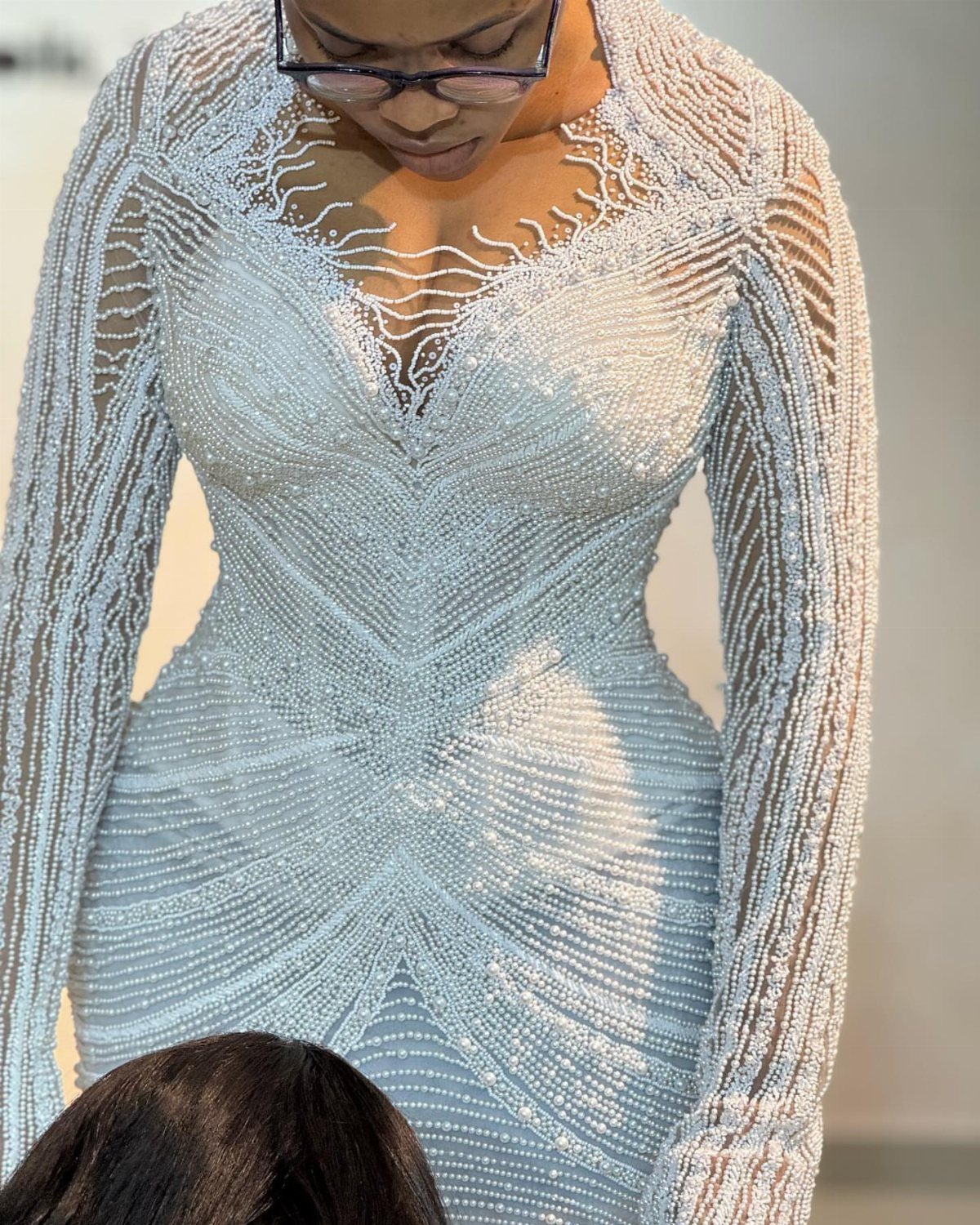 Woman wearing a form-fitting white wedding dress with intricate silver beaded patterns.