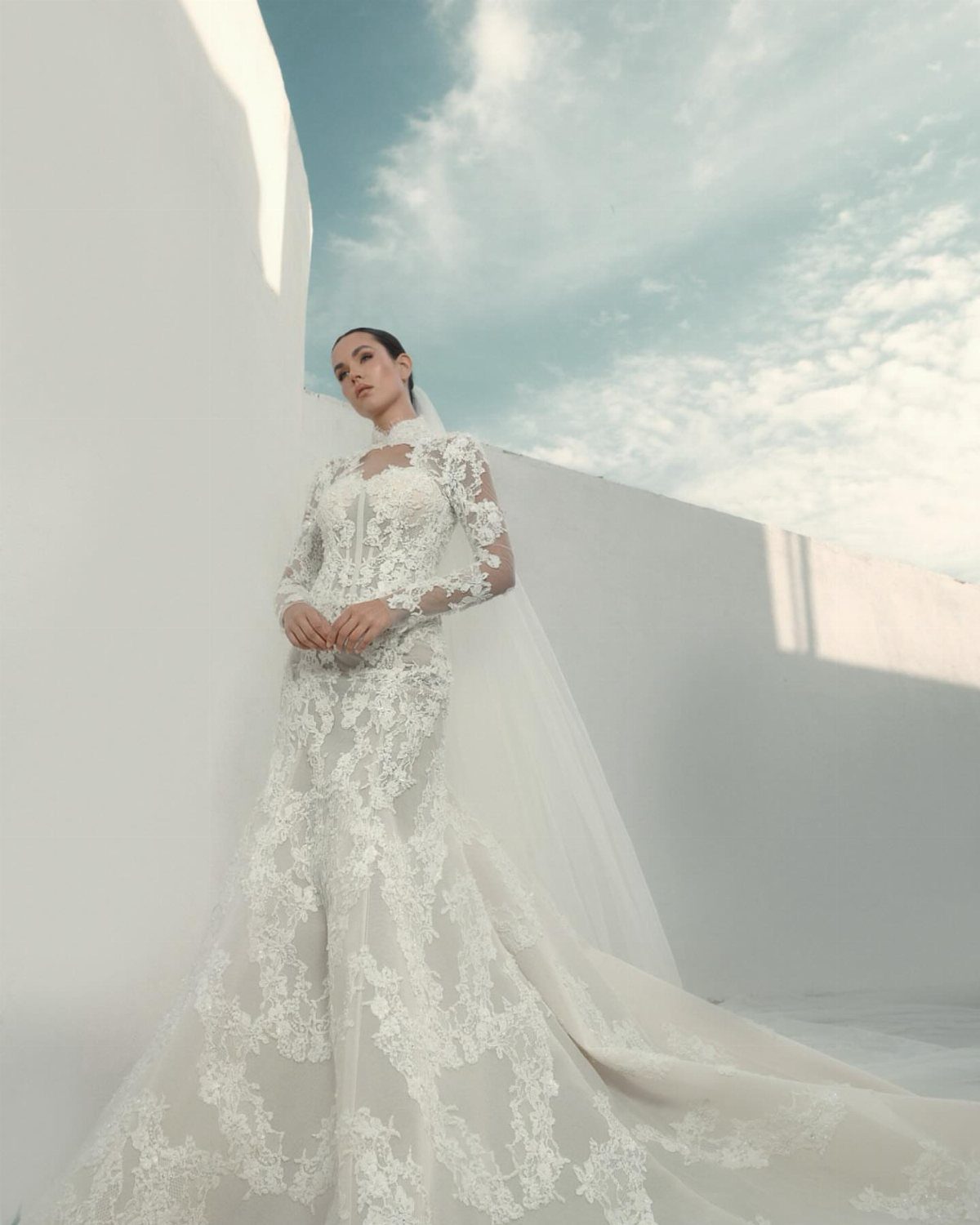 Woman in a high-neck white lace wedding dress with a long train and veil.