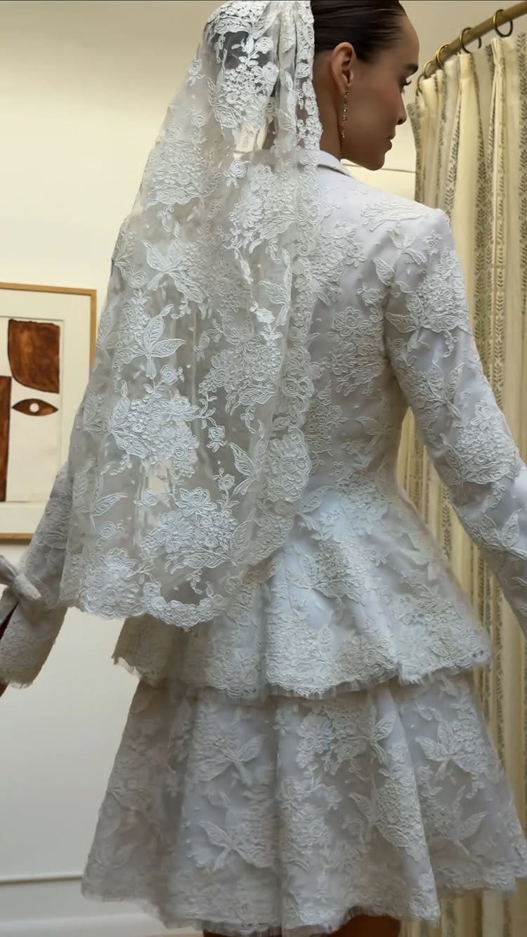 Woman wearing a white lace peplum bridal jacket, short skirt, and lace veil.