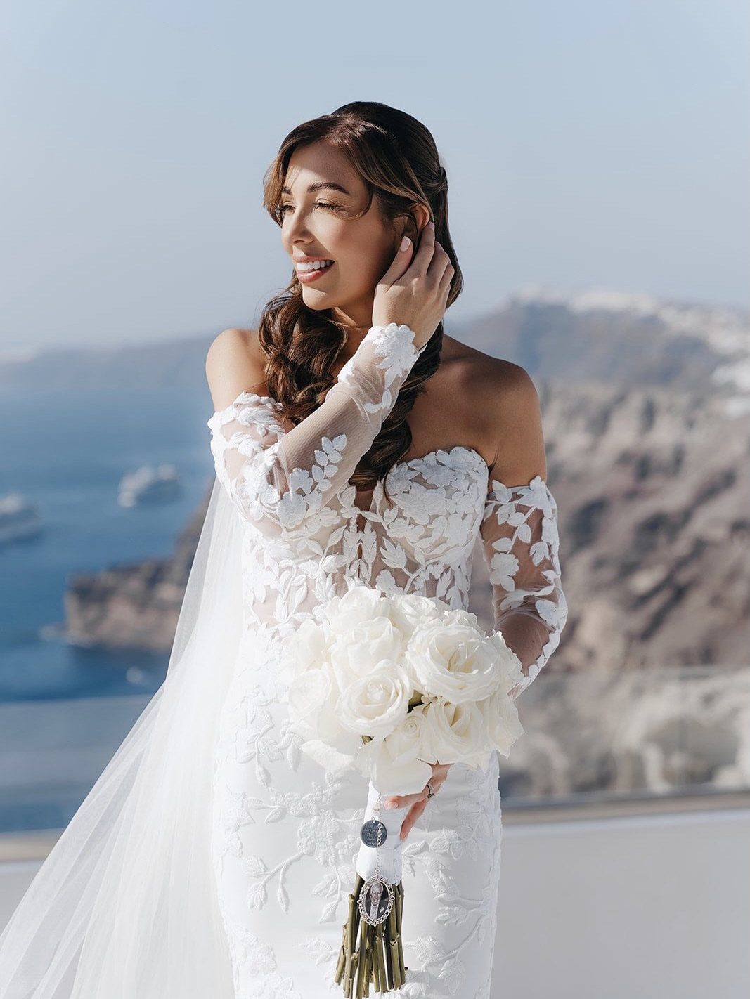Woman in a white lace wedding dress holding white roses by the coast