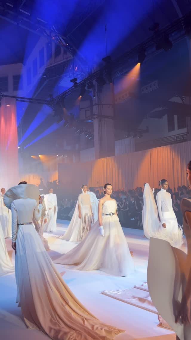 Models wearing white designer wedding dresses walking on a lit fashion runway