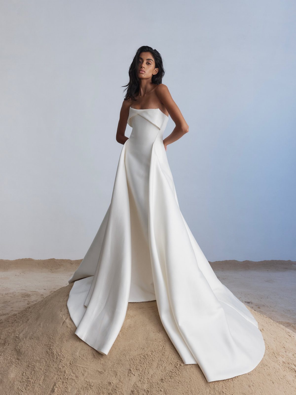 Woman in a structured white strapless wedding dress standing on a sand dune.