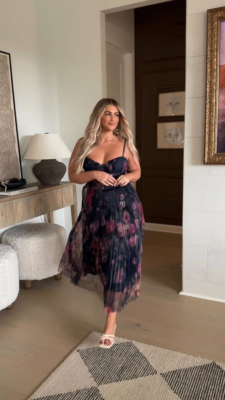 Woman wearing a dark floral midi dress and white heels in a living room.