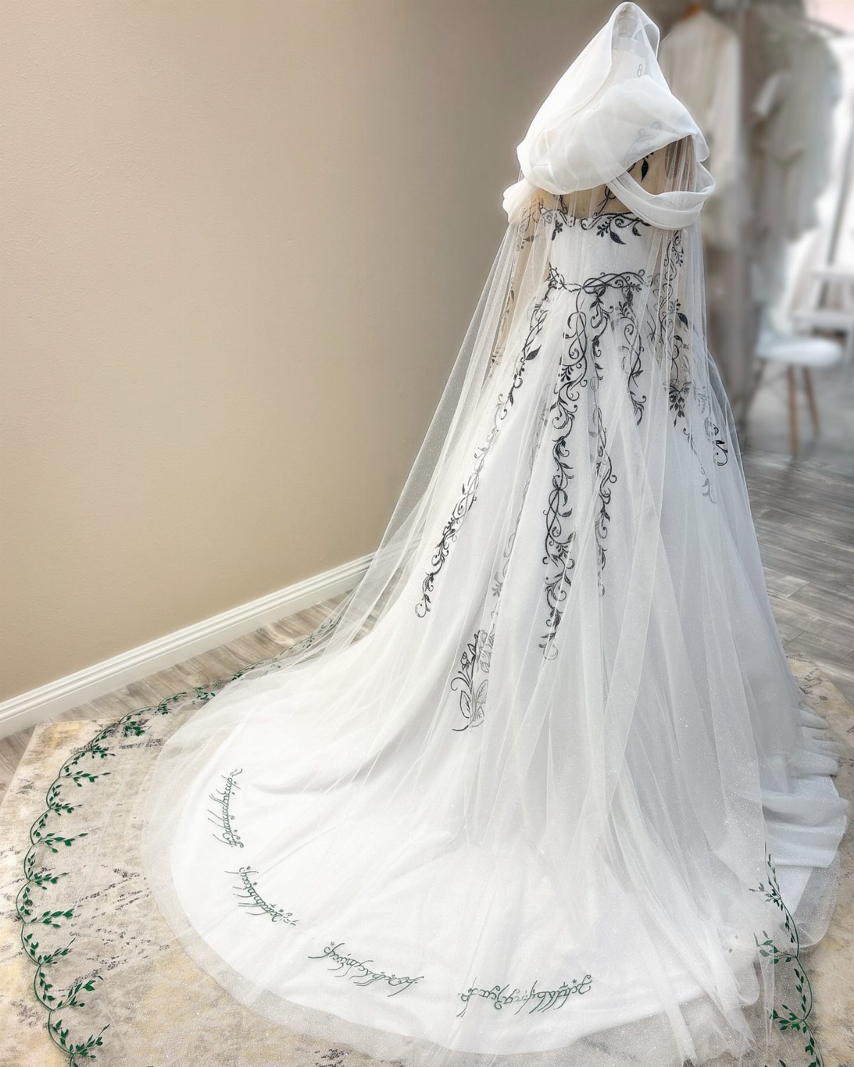 White hooded gown with green vine embroidery on the bodice and long train.